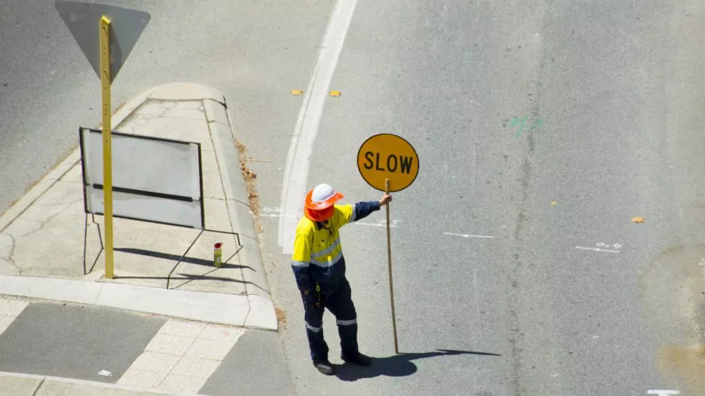 Traffic controller holding a slow sign in the middle of roadworks.